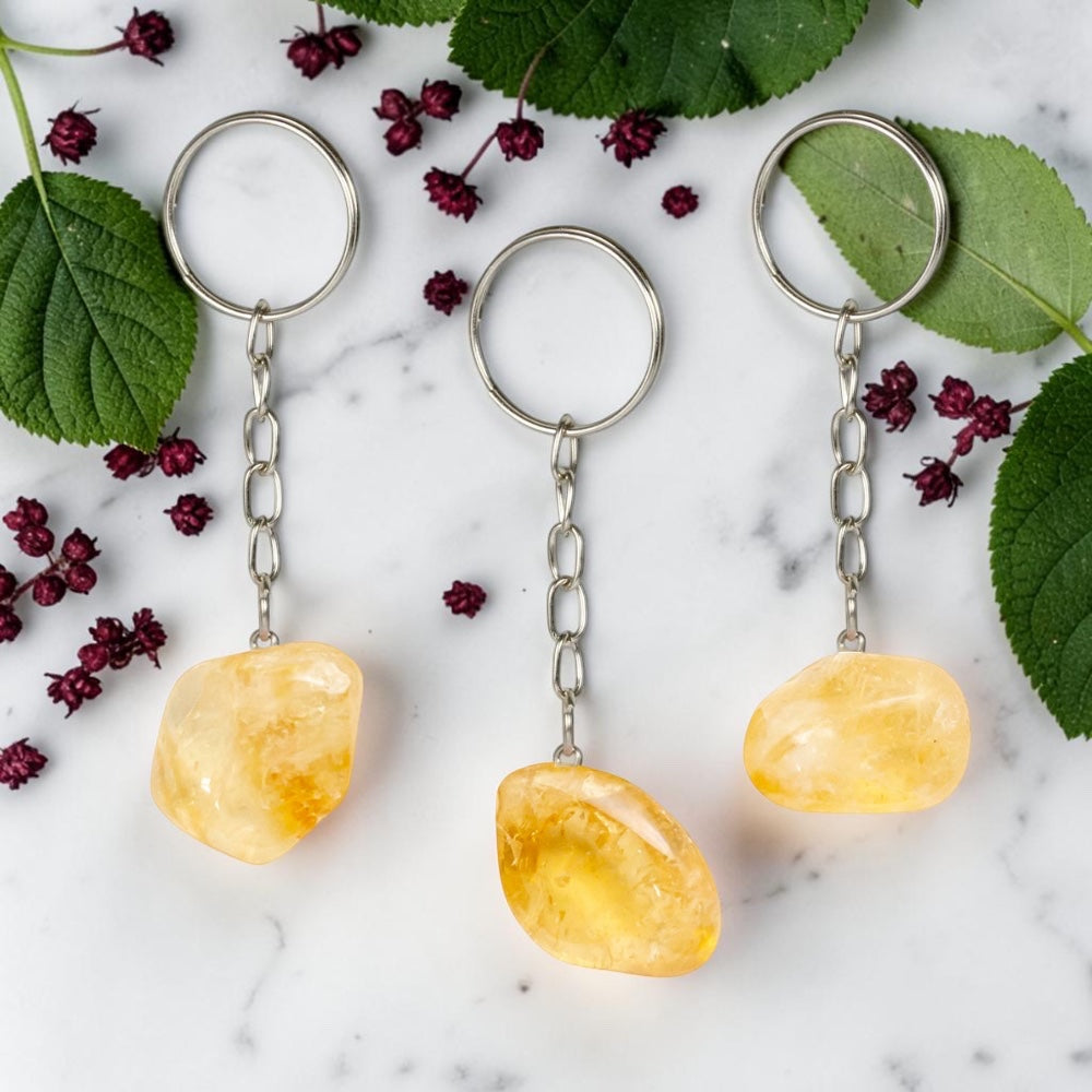 Three Citrine keychains on a marble surface with green leaves and red berries.