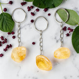 Three Citrine keychains on a marble surface with green leaves and red berries.