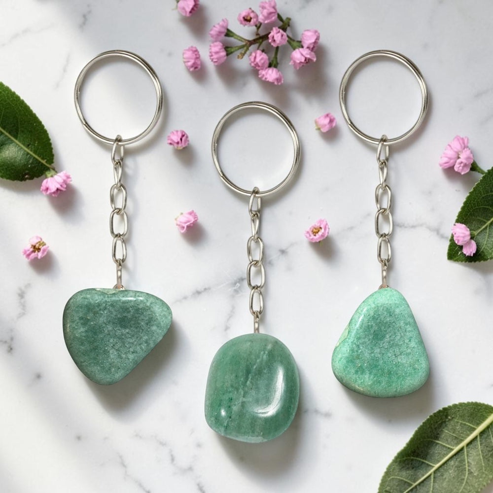 Three Green Aventurine keychains on a marble surface with pink flowers and leaves.