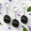 Three Black Obsidian keychains on a marble surface with purple flowers and green leaves.