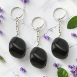 Three Black Obsidian keychains on a marble surface with purple flowers and green leaves.
