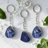 Three Sodalite keychains on a marble surface with flowers and leaves.