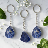 Three Sodalite keychains on a marble surface with flowers and leaves.