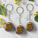 Three tiger eye keychains on a marble surface with flowers and leaves.