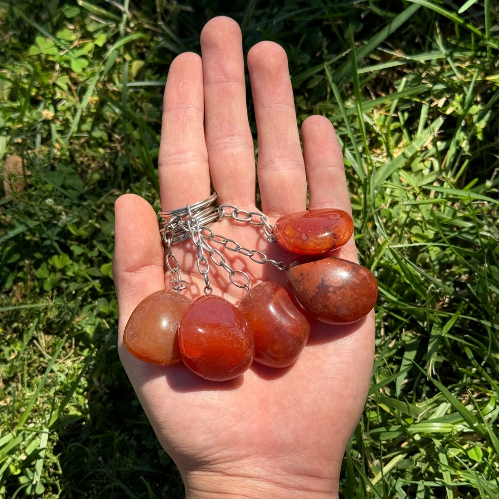Hand holding a carnelian keychain against a grassy background