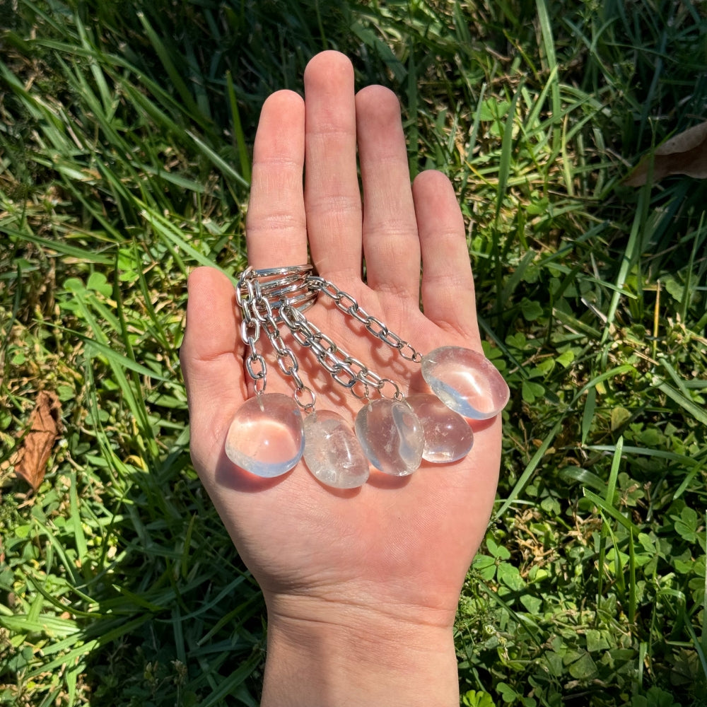 Hand holding multiple Clear Quartz keychains against a grassy background