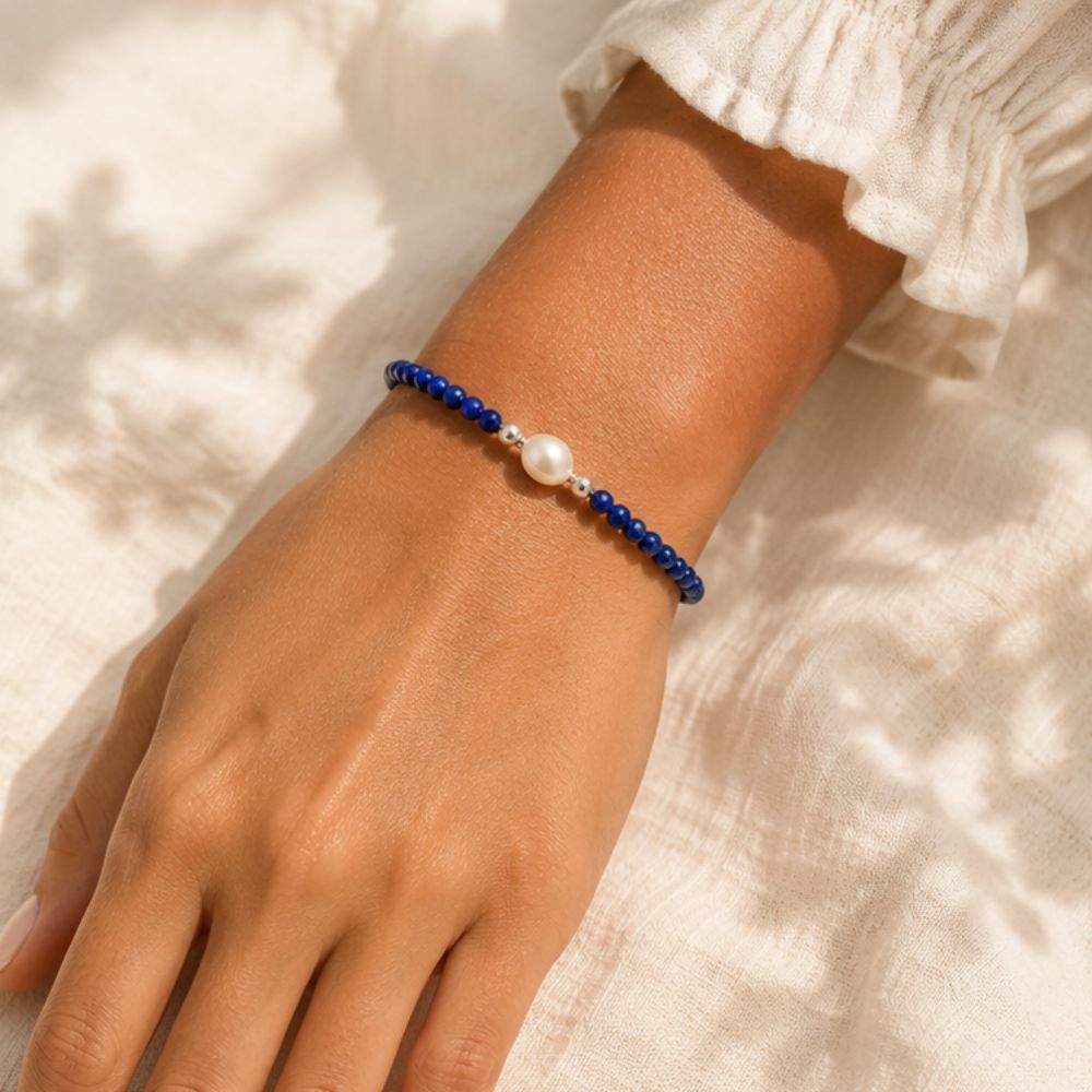 Hand wearing a blue beaded bracelet with a pearl on a light background