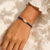 Hand wearing a blue beaded bracelet with a pearl on a light background