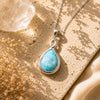 Teardrop-shaped turquoise pendant on a silver chain with a beige background