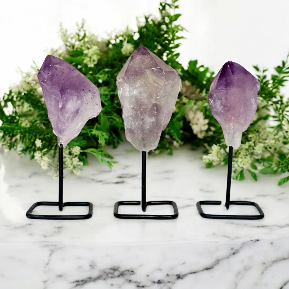 Three amethyst crystal points on stands with a floral background