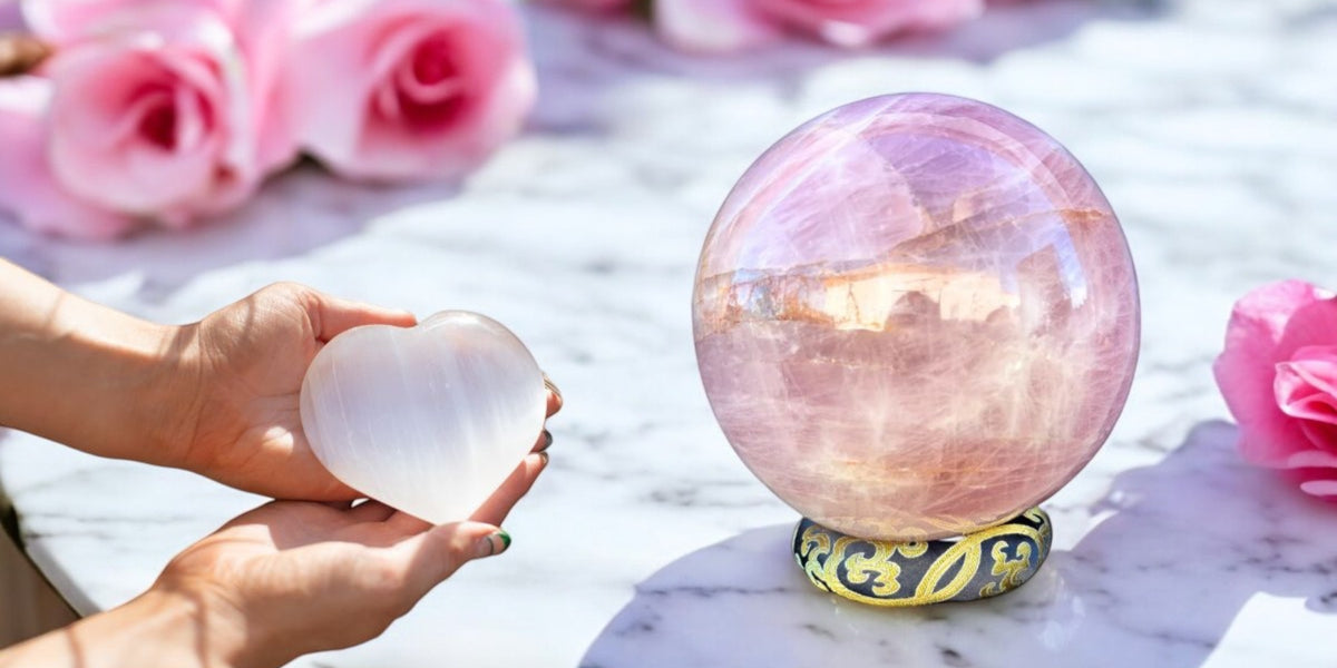 Heart-shaped crystal and rose quartz sphere on a marble surface with pink roses.