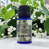 Bottle of Earths Elements Wellness Gardenia essential oil with gardenia flowers in the background