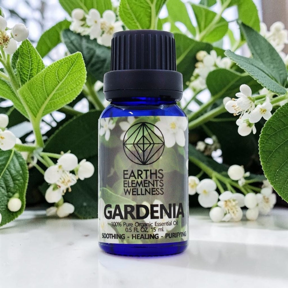 Bottle of Earths Elements Wellness Gardenia essential oil with gardenia flowers in the background