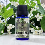 Bottle of Earths Elements Wellness Gardenia essential oil with gardenia flowers in the background