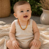 Smiling baby wearing a natural amber teething necklace with polished cognac amber beads in warm, soft natural light.