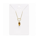 A gold necklace with a heart-shaped pendant and a dangling citrine crystal, displayed on a white card.