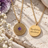 Gold mandala amethyst necklace displayed on natural stone, showing the purple amethyst pendant and reverse engraving reading “Manifesting abundance.