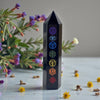 Black crystal tower with colorful symbols on a light surface with flowers and plants.