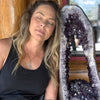 Woman leaning against a large amethyst crystal formation indoors.