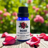 Rose essential oil bottle with red rose petals on a wooden surface and blurred floral background