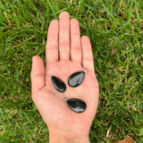 Three polished Shungite oval pendants displayed in the palm of a hand against a grass background.
