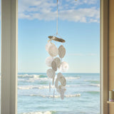 Decorative shell mobile hanging by a window with a view of the ocean.