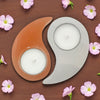 Yin and yang candle holders with candles on a wooden surface surrounded by small pink flowers.
