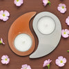Yin and yang candle holders with candles on a wooden surface surrounded by small pink flowers.