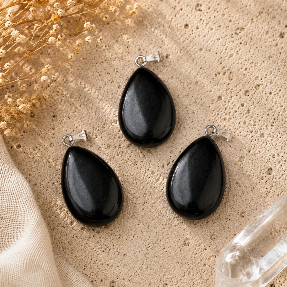 Shungite oval pendants displayed on a natural stone surface with soft linen and dried botanicals.