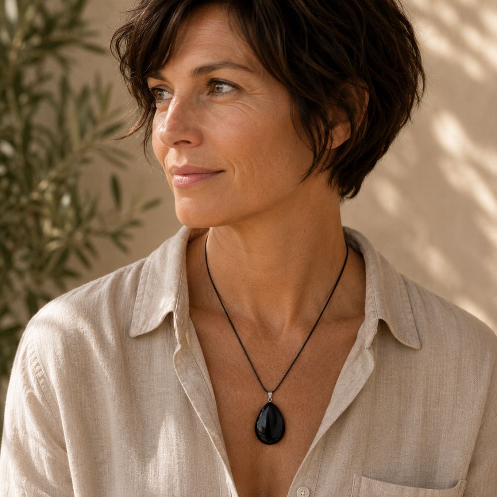 Person wearing a Shungite oval pendant on a delicate silver chain with neutral clothing in warm natural light.