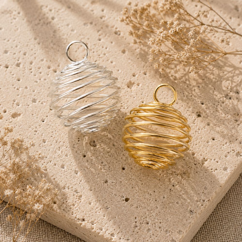 Silver and gold crystal cage pendants displayed on a natural stone surface with soft linen and dried botanicals.