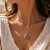 Close-up of a woman wearing a necklace with a heart-shaped purple pendant.