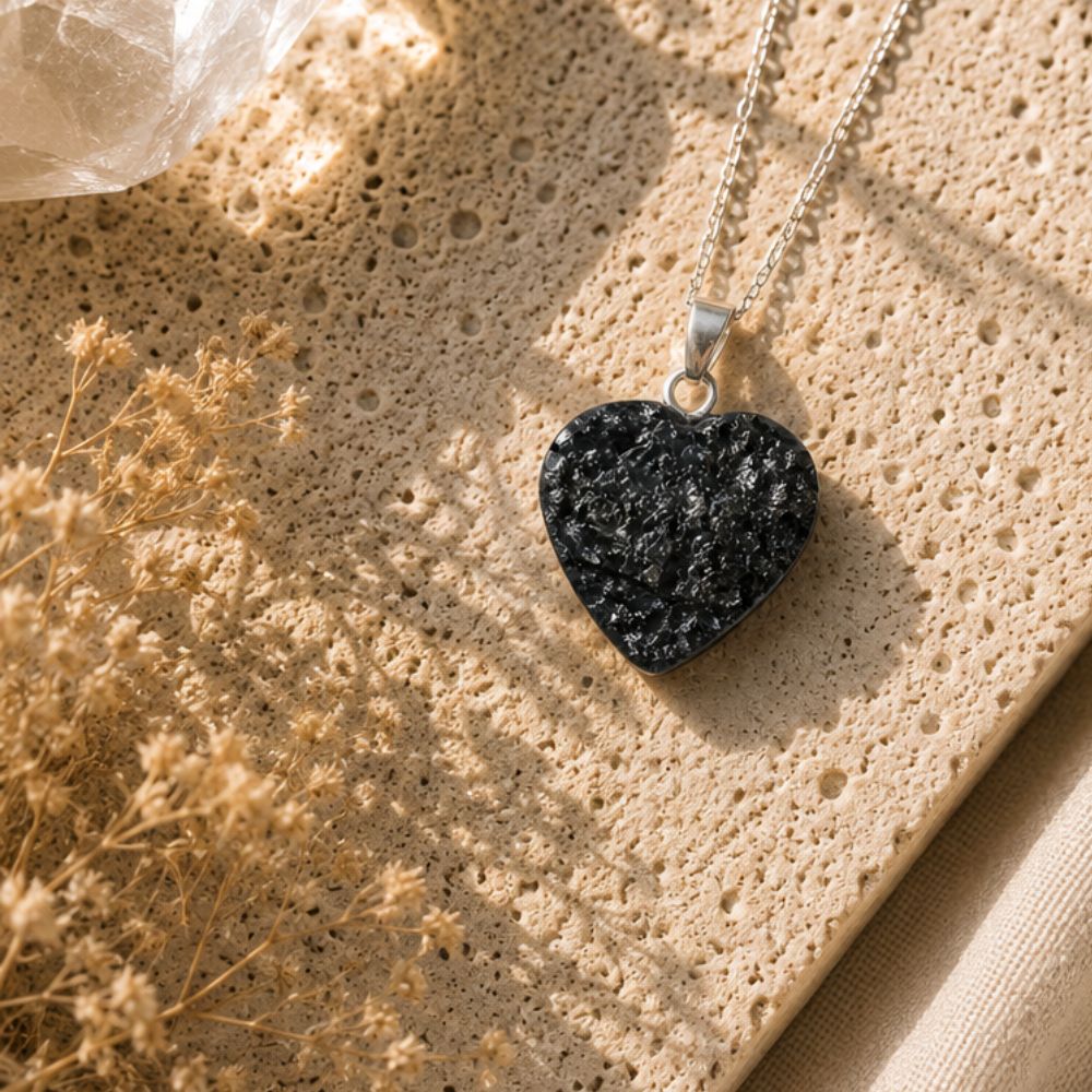 Heart-shaped black stone pendant on a chain against a textured beige surface with dried flowers.