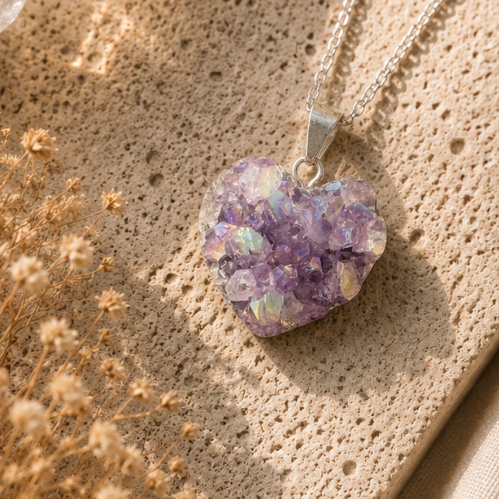 Heart-shaped purple druzy pendant on a silver chain against a textured beige background with dried flowers.