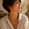 Person wearing a Chakra point pendant on a delicate silver chain with neutral clothing in warm natural light.