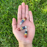 Three small cylindrical crystal bead charms with silver jump rings are resting on an open hand, set against a background of green grass.