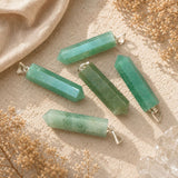 Green Aventurine point pendants displayed on a natural stone surface with soft linen and dried botanicals.