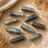 Labradorite point pendants displayed on a natural stone surface with soft linen and dried botanicals.