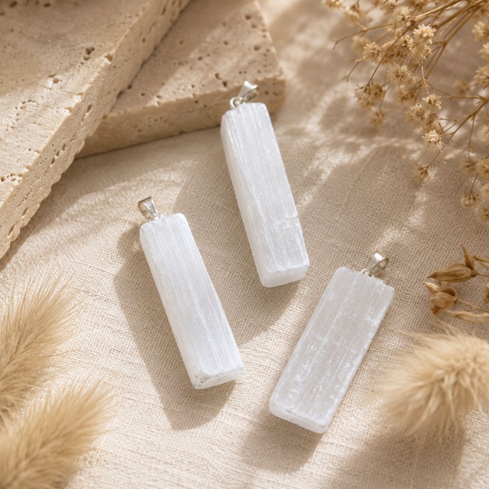 Raw Selenite point pendants displayed on soft linen with natural stone and dried botanicals.