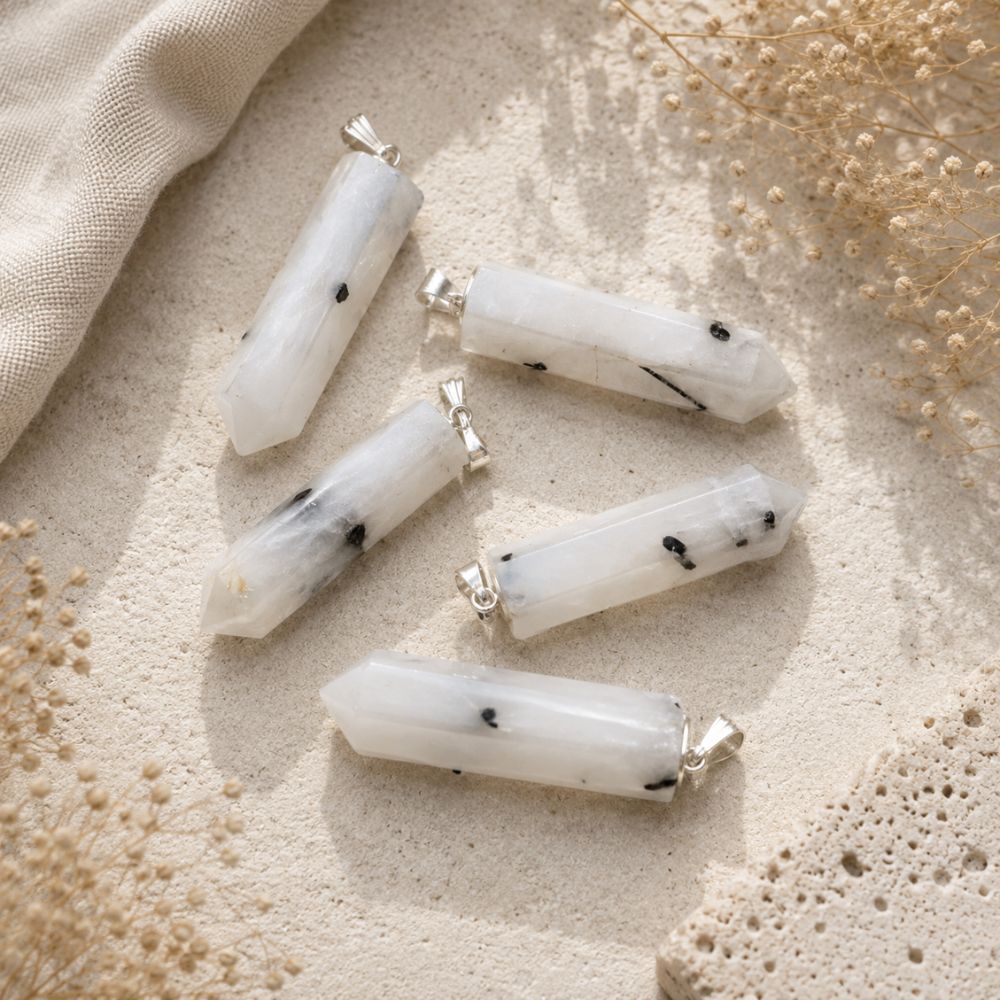 Tourmalinated Quartz crystal point pendants with silver loops on a neutral stone background.