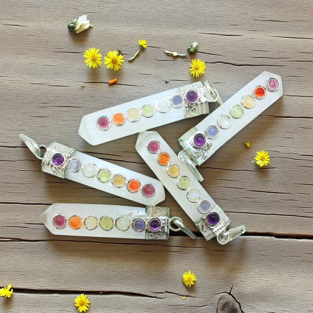 Colorful selenite pendants with gemstones on a wooden surface surrounded by small yellow flowers.