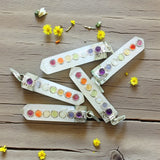 Colorful selenite pendants with gemstones on a wooden surface surrounded by small yellow flowers.