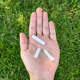 Hand holding three selenite raw pendants against a grass background