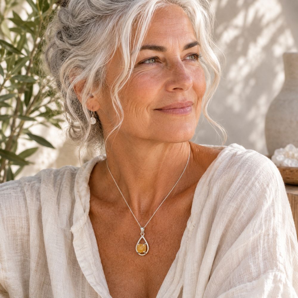 Wwoman with white hair wearing a Raw Citrine Silver Teardrop Pendant on a delicate silver chain with a soft cream linen blouse.