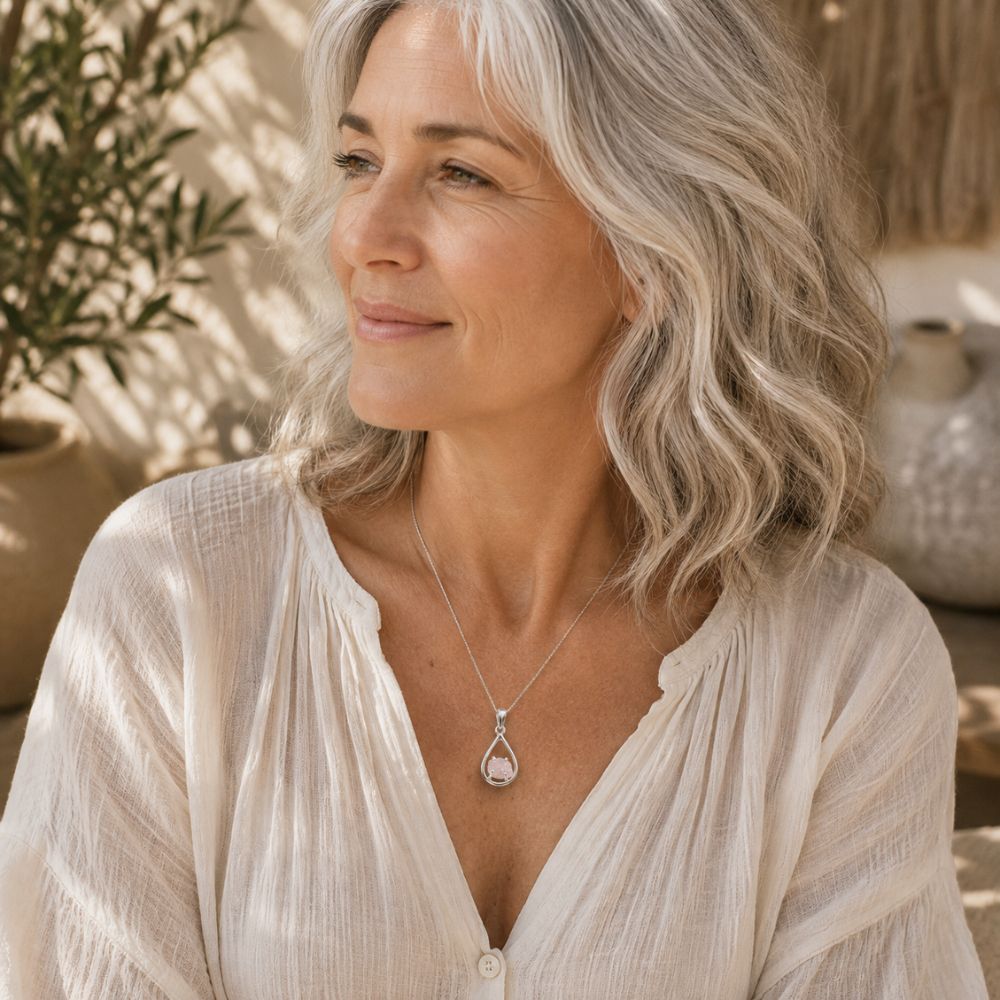 Woman with silver hair wearing a Raw Rose Quartz Silver Teardrop Pendant on a delicate silver chain with a soft cream linen blouse.