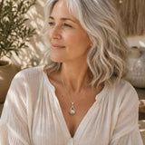 Woman with silver hair wearing a Raw Rose Quartz Silver Teardrop Pendant on a delicate silver chain with a soft cream linen blouse.