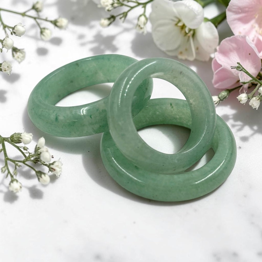 Three green aventurine rings on a white marble surface with flowers in the background