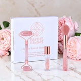 Beauty tool set with roller, brush, and bottle in front of 'Earth's Elements' packaging with pink flowers in the background.
