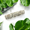 Sage bundle tied with twine on a white surface with green leaves in the background