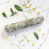 Sage bundle on a marble surface with scattered leaves and flowers